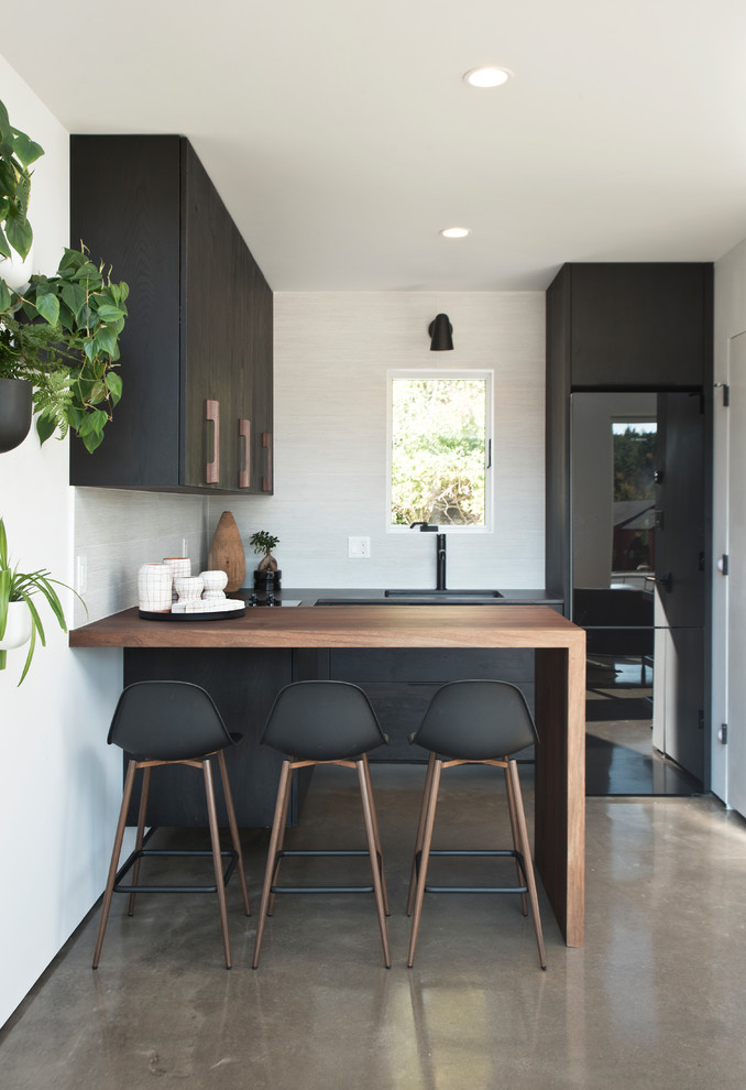 Inspiration for a scandinavian u-shaped kitchen in New York with an undermount sink, flat-panel cabinets, white splashback, black appliances, concrete floors, a peninsula, grey floor and black benchtop.