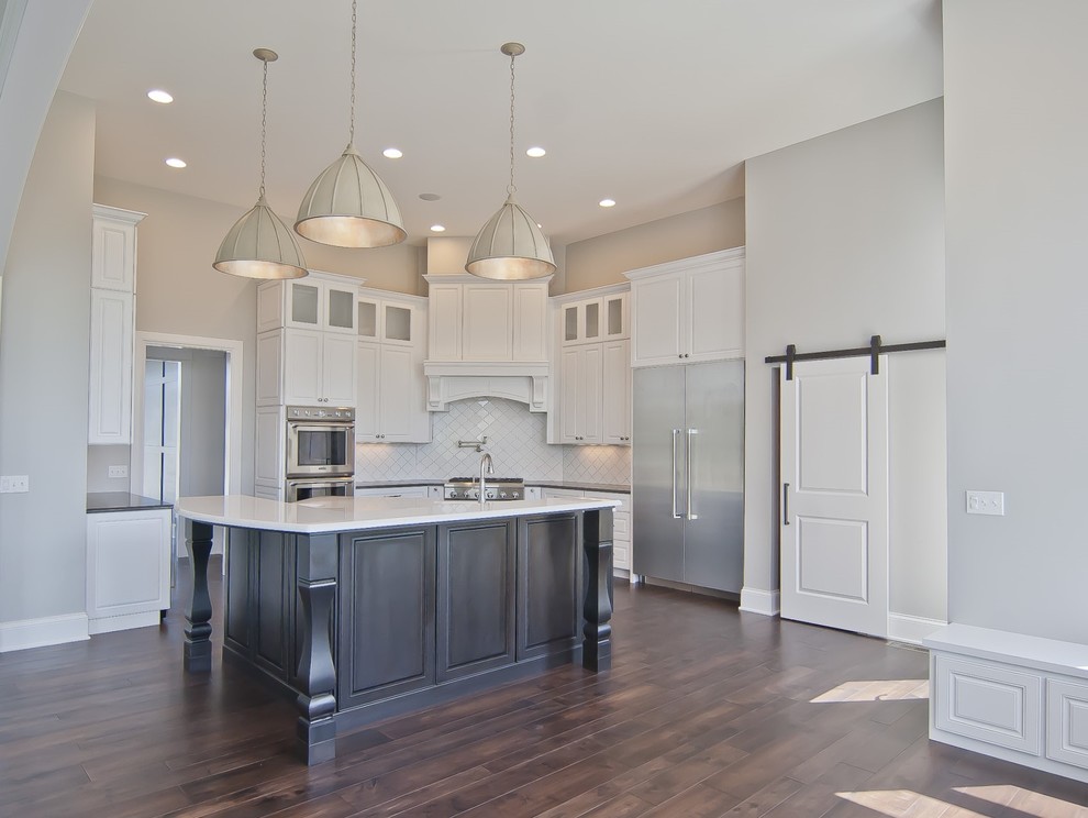 Inspiration for a transitional medium tone wood floor kitchen remodel with a farmhouse sink, white cabinets, quartz countertops, white backsplash, ceramic backsplash, stainless steel appliances, an island and white countertops
