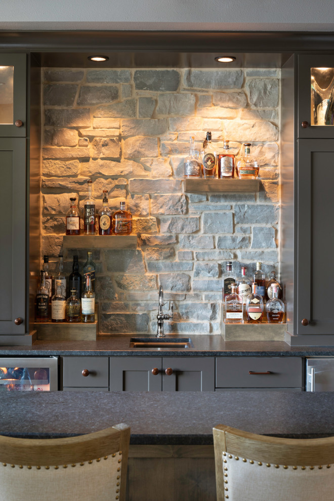 Design ideas for a mid-sized transitional wet bar in Milwaukee with an undermount sink, flat-panel cabinets, brown cabinets, granite benchtops, multi-coloured splashback, limestone splashback, dark hardwood floors, brown floor and black benchtop.