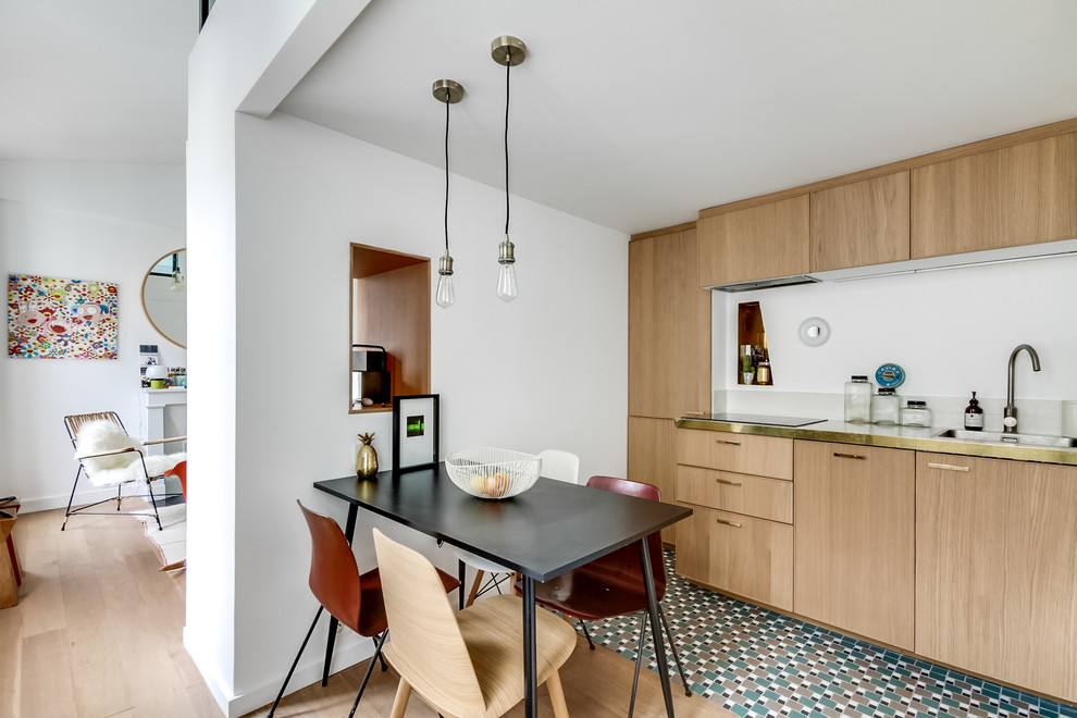 This is an example of a mid-sized contemporary single-wall eat-in kitchen in Paris with a drop-in sink, flat-panel cabinets, light wood cabinets, stainless steel benchtops, light hardwood floors, no island, white splashback and panelled appliances.