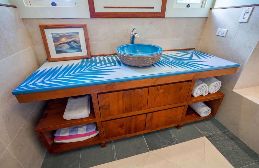 Photo of a mid-sized beach style 3/4 bathroom in Hawaii with a two-piece toilet, beige tile, open cabinets, medium wood cabinets, an alcove tub, a shower/bathtub combo, ceramic tile, beige walls, ceramic floors, a vessel sink, concrete benchtops, beige floor, a shower curtain and blue benchtops.