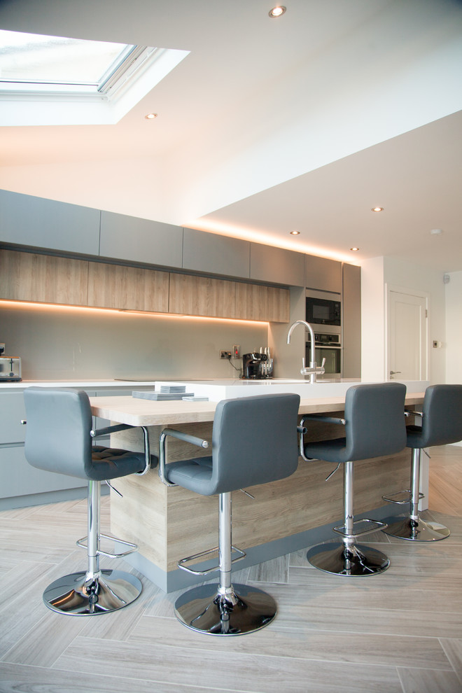 Design ideas for a mid-sized contemporary single-wall open plan kitchen in Dublin with quartzite benchtops, porcelain floors, with island, beige floor, flat-panel cabinets, beige splashback, glass sheet splashback and stainless steel appliances.
