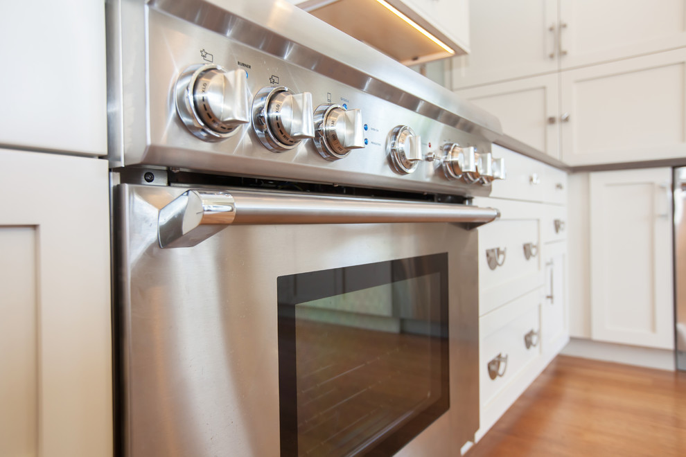 Inspiration for a large transitional l-shaped medium tone wood floor eat-in kitchen remodel in Boston with an undermount sink, shaker cabinets, white cabinets, quartz countertops, gray backsplash, glass sheet backsplash, stainless steel appliances and an island