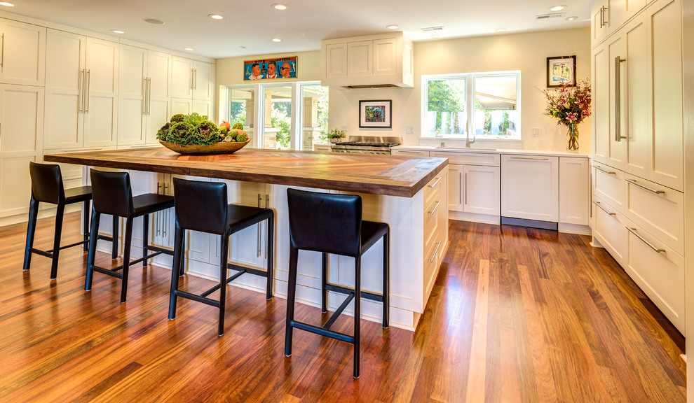 Design ideas for a large contemporary u-shaped open plan kitchen in Milwaukee with white cabinets, wood benchtops, stainless steel appliances, medium hardwood floors, with island, an undermount sink, recessed-panel cabinets, brown floor and brown benchtop.