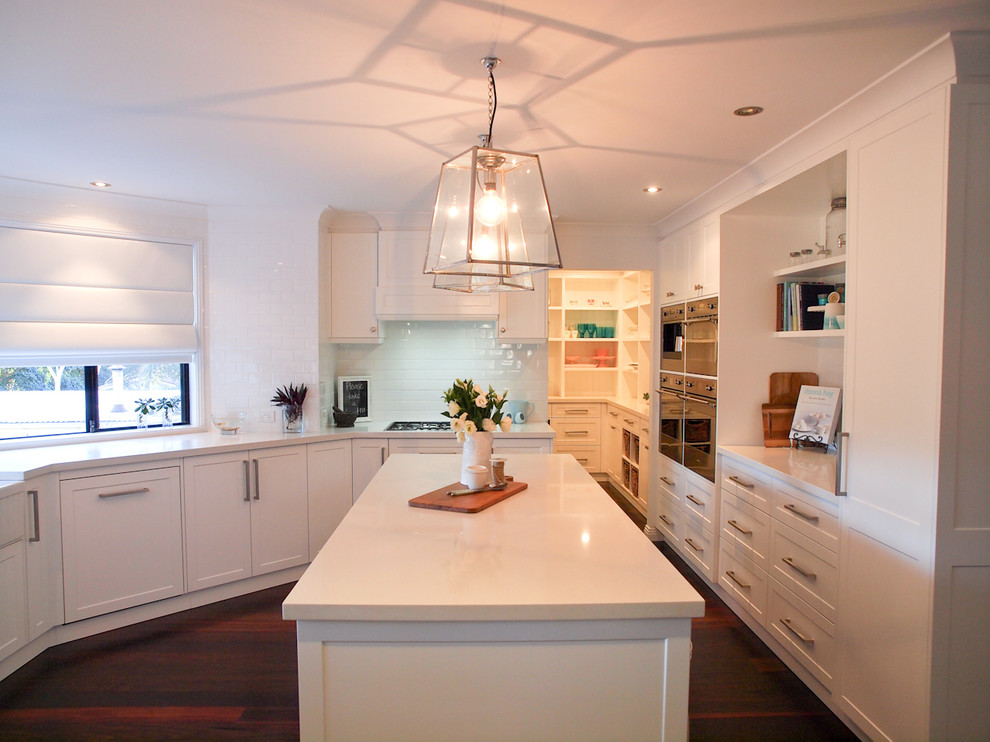 Design ideas for a mid-sized traditional u-shaped separate kitchen in Wollongong with shaker cabinets, white cabinets, white splashback, subway tile splashback, dark hardwood floors, with island, a farmhouse sink, quartz benchtops and stainless steel appliances.