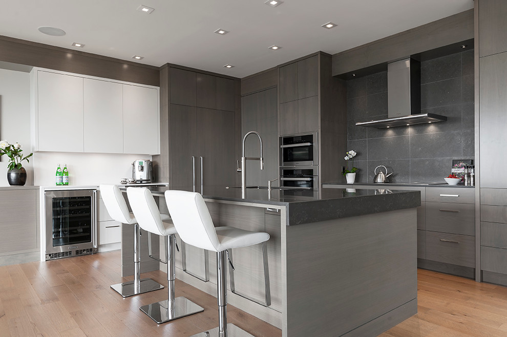 This is an example of a mid-sized contemporary kitchen in Vancouver with an undermount sink, flat-panel cabinets, grey cabinets, quartz benchtops, grey splashback, ceramic splashback, stainless steel appliances, with island and light hardwood floors.