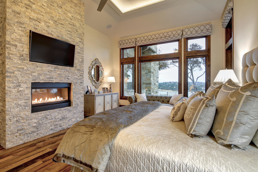 Design ideas for an expansive transitional master bedroom in Austin with white walls, light hardwood floors, a ribbon fireplace, a stone fireplace surround and multi-coloured floor.