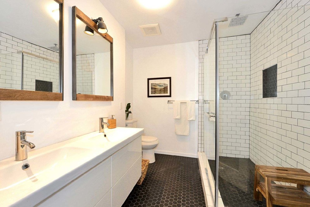 Inspiration for a contemporary master bathroom in Los Angeles with flat-panel cabinets, white cabinets, a corner shower, a two-piece toilet, white tile, subway tile, white walls, mosaic tile floors, an integrated sink, black floor, a hinged shower door and white benchtops.