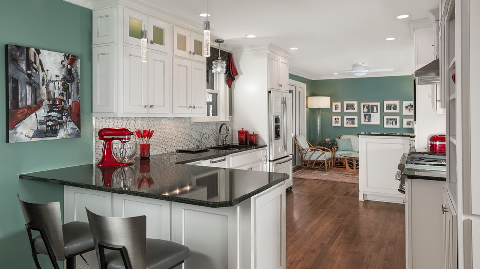 This is an example of a transitional l-shaped open plan kitchen in Nashville with white cabinets, quartz benchtops, metallic splashback, glass tile splashback, panelled appliances, medium hardwood floors, a peninsula, an undermount sink and recessed-panel cabinets.