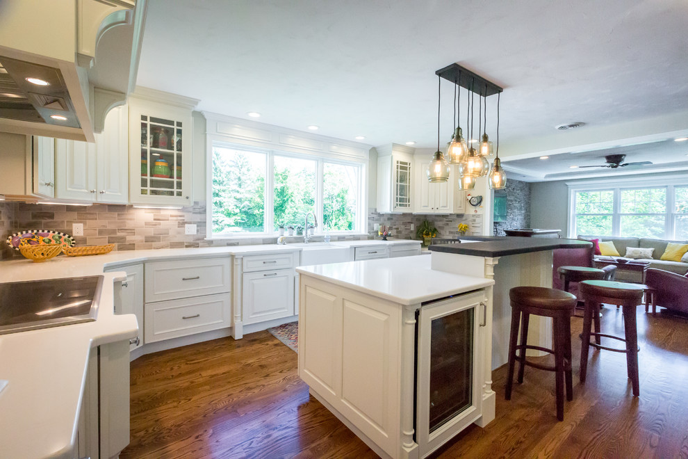 Eat-in kitchen - mid-sized transitional u-shaped medium tone wood floor eat-in kitchen idea in Boston with raised-panel cabinets, white cabinets, an island, a farmhouse sink, quartz countertops, gray backsplash, stone tile backsplash and paneled appliances