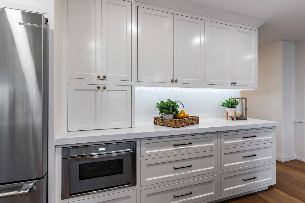 Klassisk inredning av ett mellanstort vit vitt kök, med en enkel diskho, luckor med infälld panel, gula skåp, bänkskiva i kvarts, vitt stänkskydd, stänkskydd i keramik, rostfria vitvaror, mellanmörkt trägolv, en köksö och brunt golv