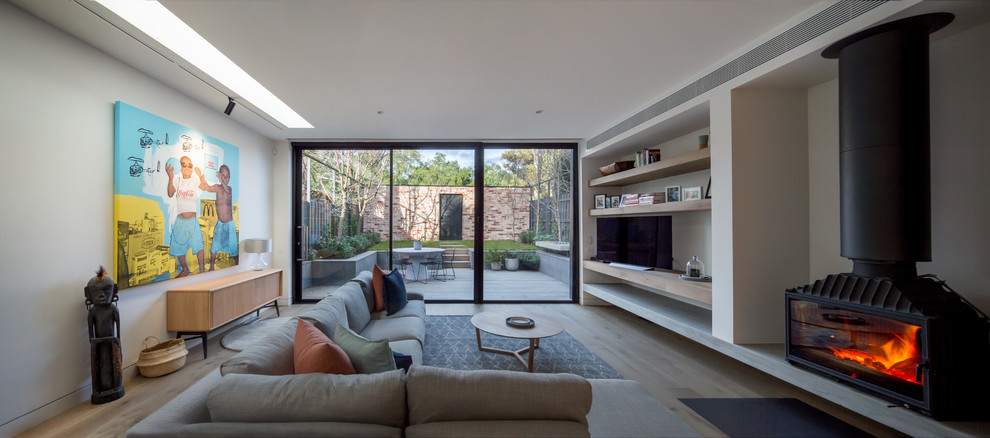 Contemporary living room in Melbourne with white walls, medium hardwood floors, a hanging fireplace and brown floor.