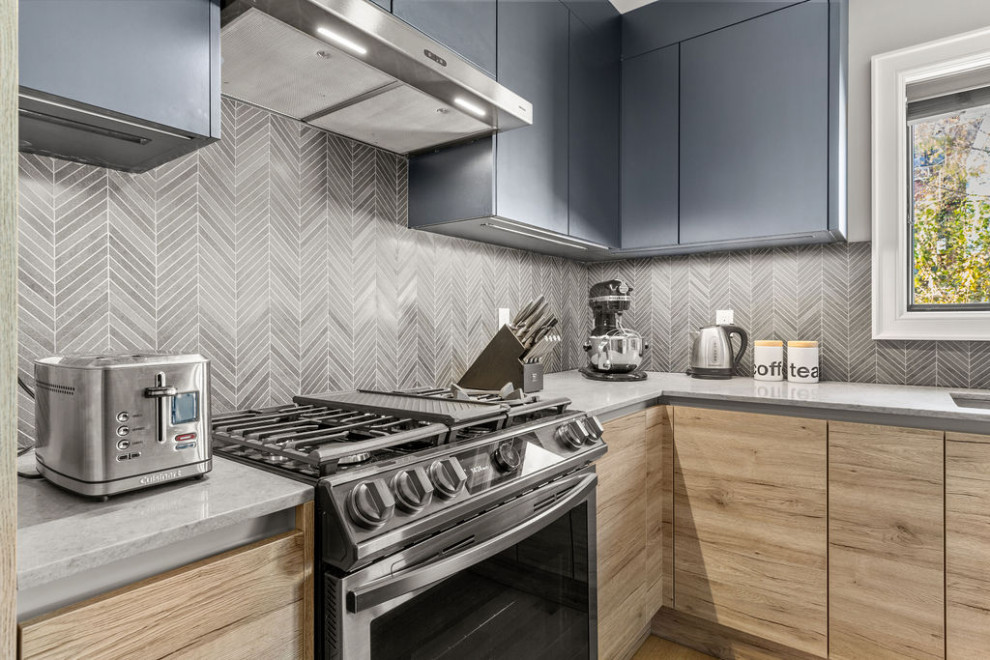 Foto di una cucina minimalista di medie dimensioni con lavello sottopiano, ante lisce, ante in legno chiaro, top in superficie solida, paraspruzzi grigio, paraspruzzi con piastrelle a mosaico, elettrodomestici neri, pavimento in compensato, pavimento beige e top grigio
