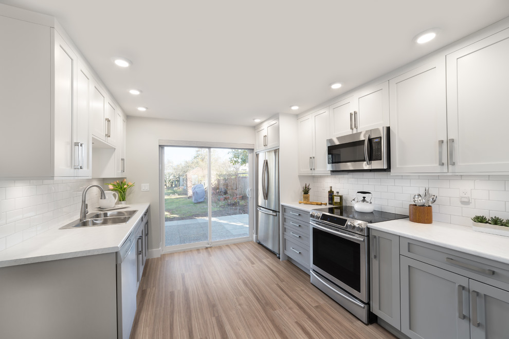 Example of a mid-sized transitional galley vinyl floor eat-in kitchen design in Vancouver with a double-bowl sink, shaker cabinets, gray cabinets, laminate countertops, white backsplash, subway tile backsplash, stainless steel appliances and a peninsula