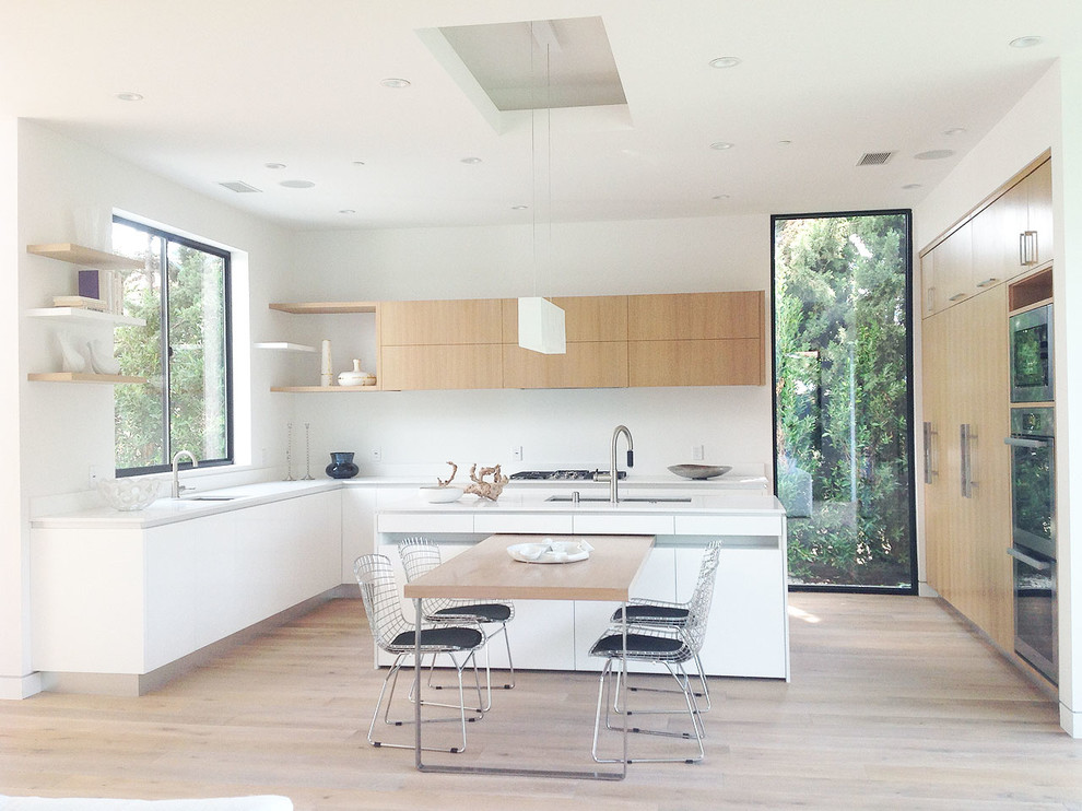 Photo of a mid-sized contemporary u-shaped eat-in kitchen in Los Angeles with a drop-in sink, flat-panel cabinets, white cabinets, soapstone benchtops, white splashback, stone tile splashback, stainless steel appliances, light hardwood floors and with island.