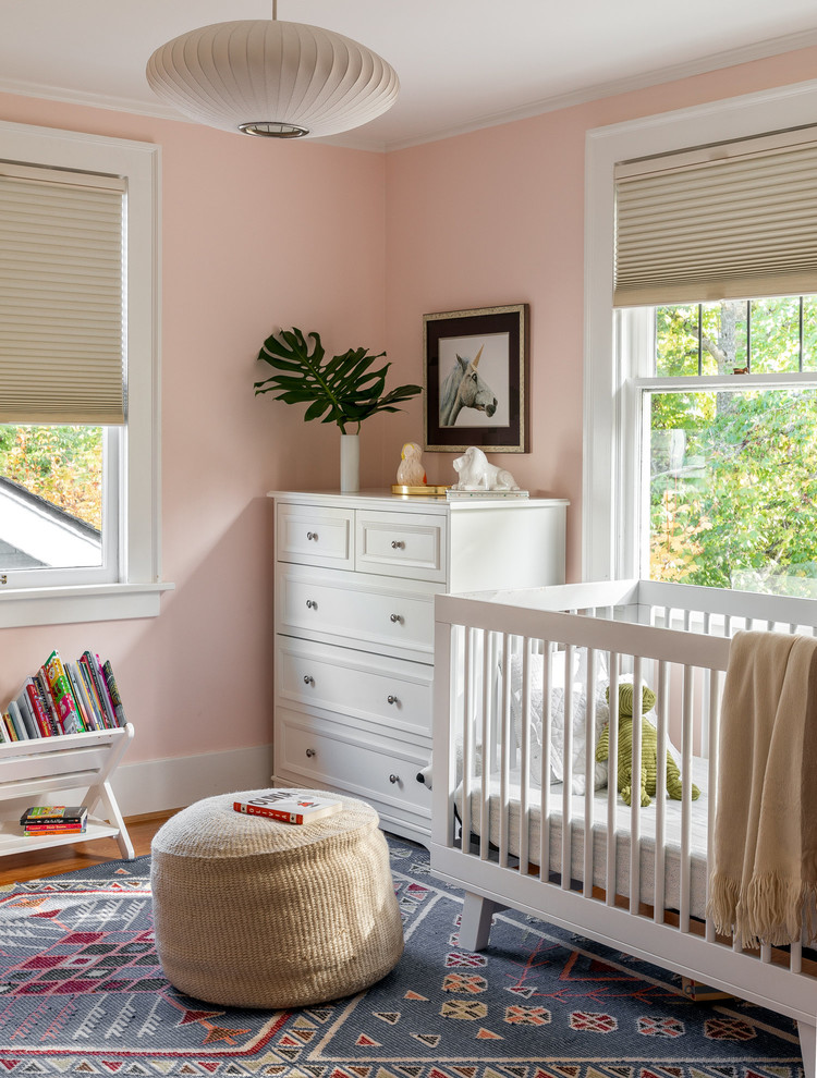Photo of a transitional nursery for girls in Portland with pink walls, medium hardwood floors and brown floor.