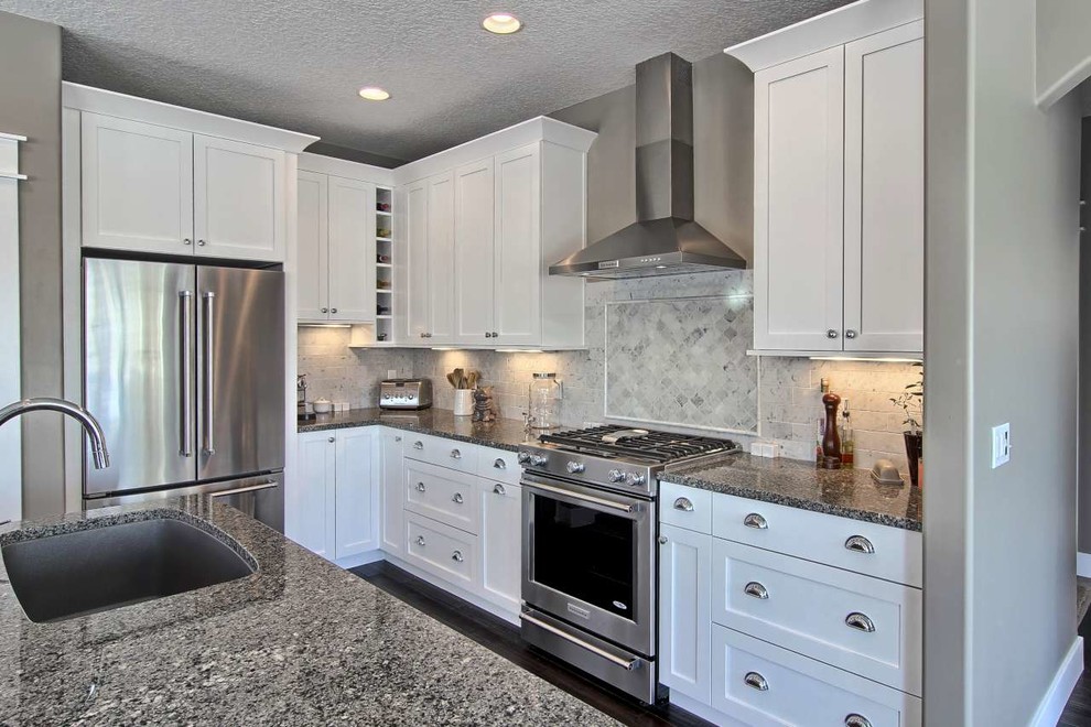 Inspiration for a mid-sized transitional l-shaped dark wood floor open concept kitchen remodel with a single-bowl sink, shaker cabinets, white cabinets, granite countertops, gray backsplash, stone tile backsplash, stainless steel appliances and an island