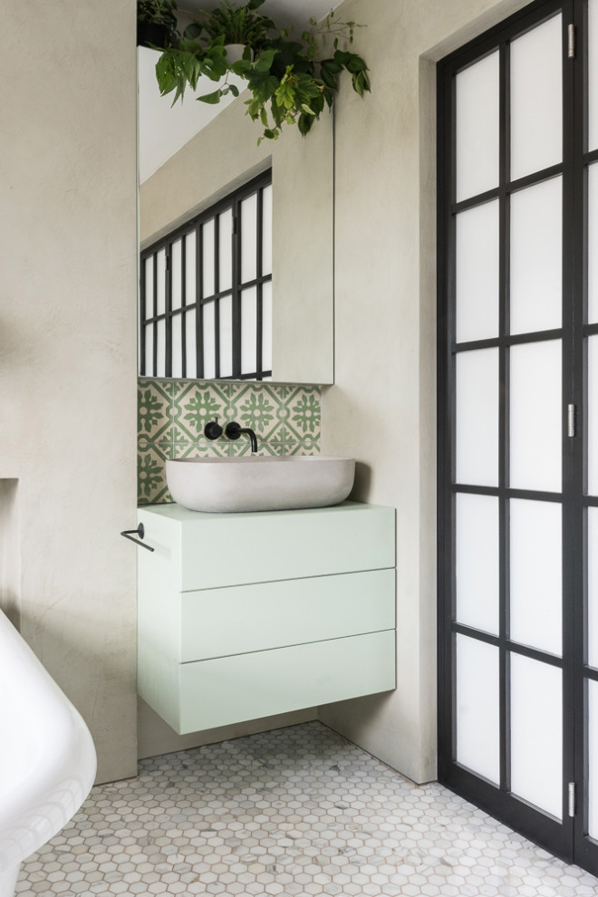This is an example of a mid-sized modern master bathroom in London with flat-panel cabinets, green cabinets, a freestanding tub, a curbless shower, a one-piece toilet, green tile, cement tile, grey walls, marble floors, a console sink, wood benchtops, white floor, a sliding shower screen and green benchtops.