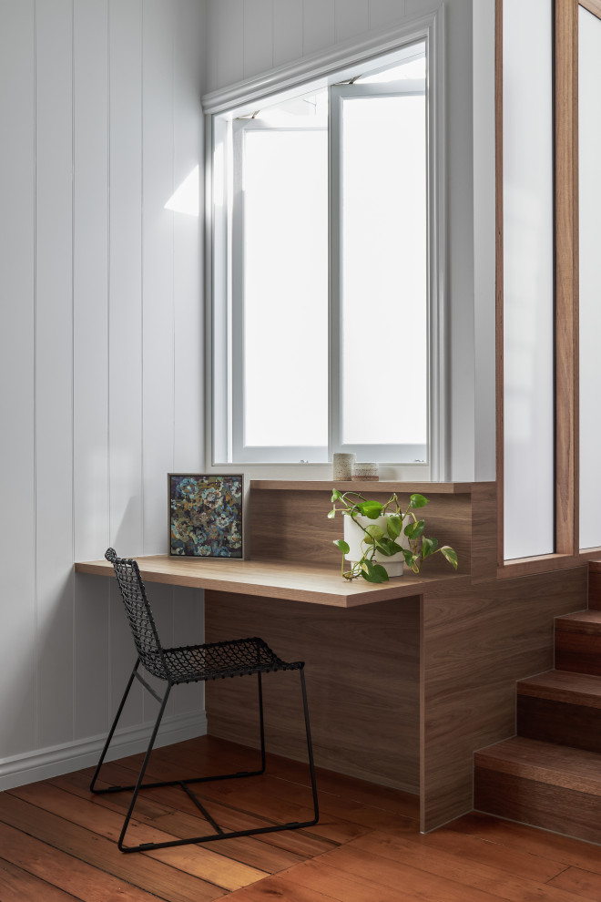 Modelo de despacho moderno con paredes blancas, suelo de madera en tonos medios, escritorio empotrado, suelo marrón y machihembrado