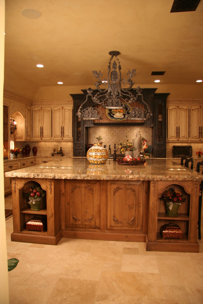 This is an example of a mid-sized mediterranean single-wall eat-in kitchen in Oklahoma City with an undermount sink, raised-panel cabinets, dark wood cabinets, marble benchtops, beige splashback, stone tile splashback, black appliances, travertine floors and with island.