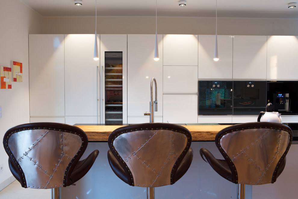 Zweizeilige, Geräumige Moderne Wohnküche mit integriertem Waschbecken, flächenbündigen Schrankfronten, weißen Schränken, Granit-Arbeitsplatte, schwarzen Elektrogeräten, dunklem Holzboden, Kücheninsel, braunem Boden und schwarzer Arbeitsplatte in Hamburg