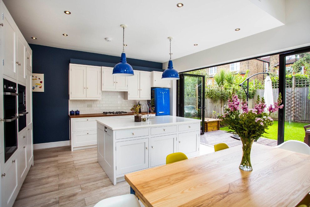 Photo of a large contemporary l-shaped eat-in kitchen in London with white cabinets, white splashback, subway tile splashback, light hardwood floors, with island, an undermount sink, shaker cabinets, quartz benchtops and black appliances.