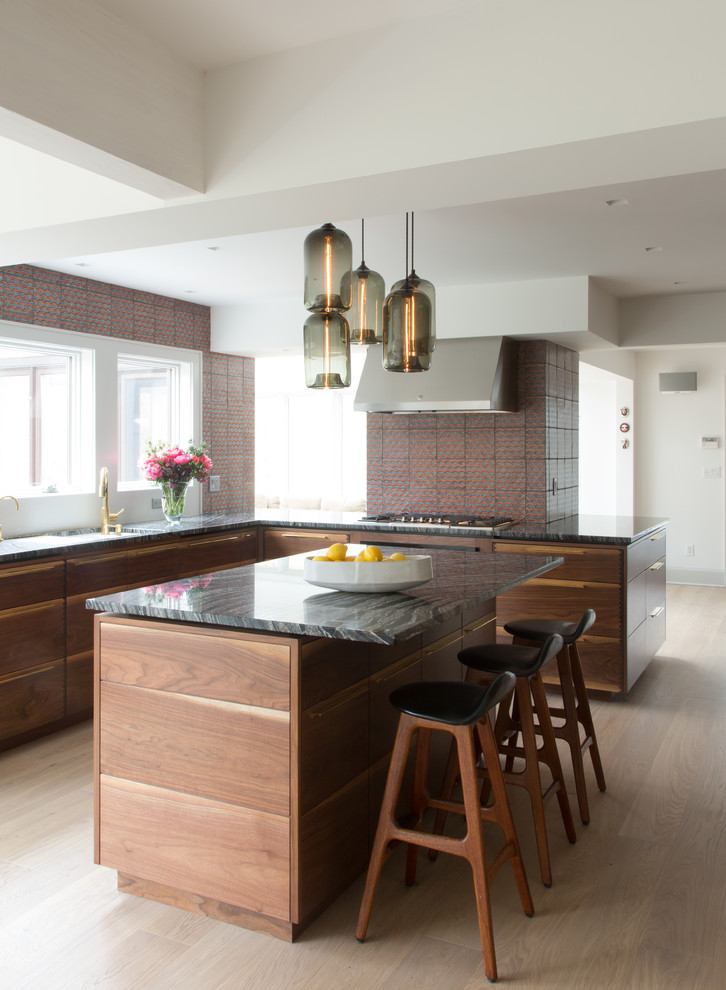 This is an example of a mid-sized modern l-shaped open plan kitchen in New York with an undermount sink, flat-panel cabinets, medium wood cabinets, multi-coloured splashback, terra-cotta splashback, black appliances, light hardwood floors, with island, onyx benchtops and multi-coloured benchtop.
