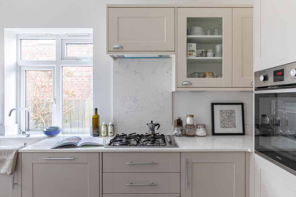 This is an example of a small scandinavian l-shaped separate kitchen in London with a drop-in sink, shaker cabinets, beige cabinets, quartzite benchtops, white splashback, no island and white benchtop.