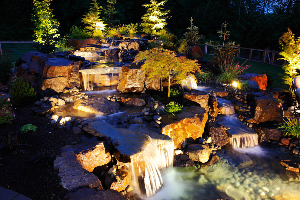 This is an example of a country backyard garden in Seattle with a water feature and river rock.