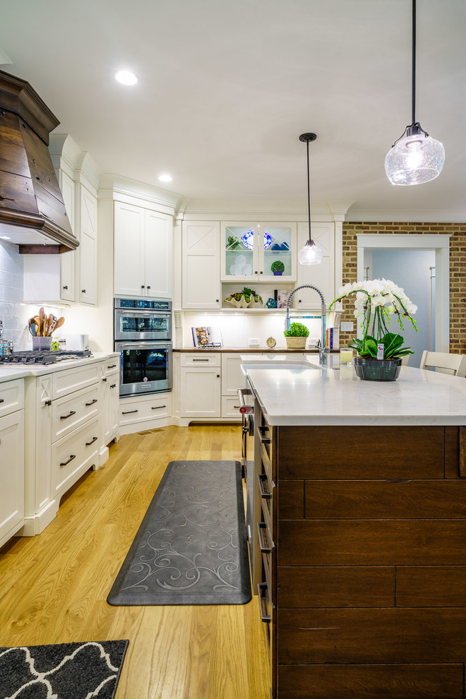 Large transitional u-shaped medium tone wood floor and brown floor eat-in kitchen photo with a farmhouse sink, recessed-panel cabinets, white cabinets, quartz countertops, white backsplash, ceramic backsplash, stainless steel appliances, an island and white countertops
