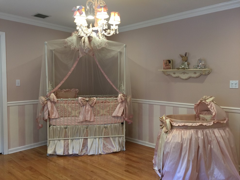 Design ideas for a large traditional nursery for girls in New York with pink walls and light hardwood floors.