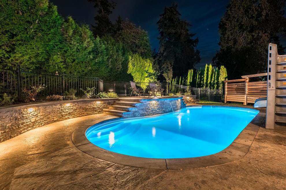 This is an example of a large traditional backyard kidney-shaped natural pool in Vancouver with a water slide and stamped concrete.