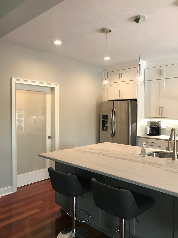 Mid-sized transitional single-wall medium tone wood floor and brown floor eat-in kitchen photo with an undermount sink, shaker cabinets, white cabinets, quartzite countertops, gray backsplash, glass tile backsplash, stainless steel appliances, an island and multicolored countertops