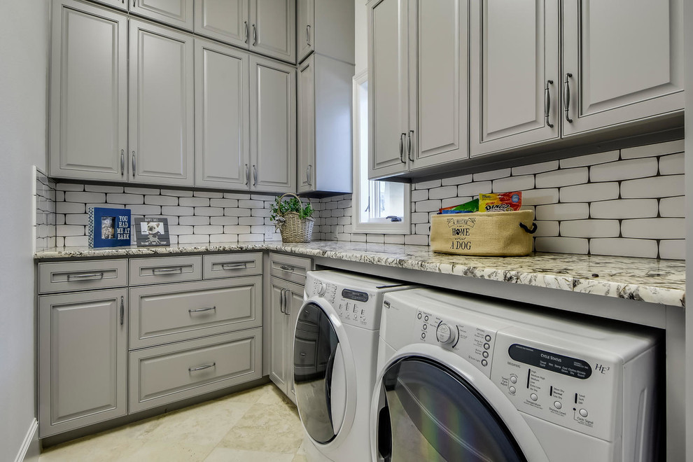 Photo of a large mediterranean u-shaped utility room in Austin with an undermount sink, raised-panel cabinets, grey cabinets, granite benchtops, grey walls, travertine floors and a side-by-side washer and dryer.