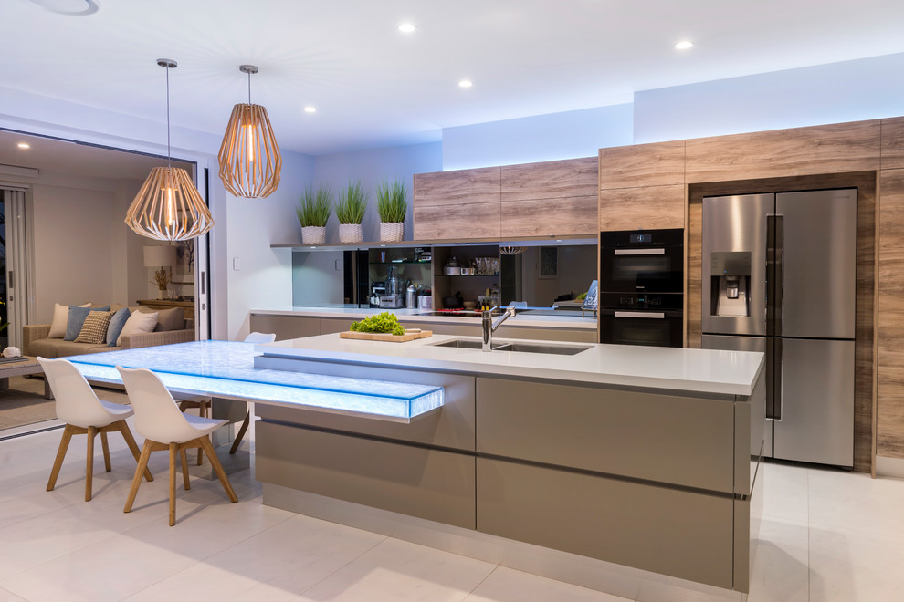 Mid-sized contemporary galley open plan kitchen in Brisbane with a double-bowl sink, flat-panel cabinets, glass benchtops, mirror splashback, beige floor, medium wood cabinets, black appliances, with island and grey benchtop.