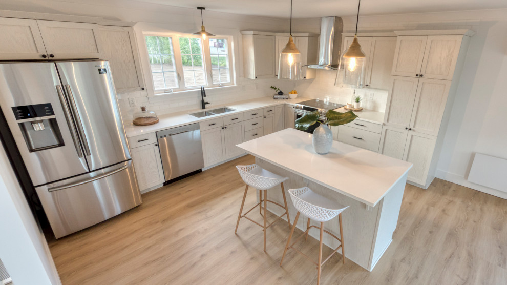 Photo of a mid-sized beach style l-shaped eat-in kitchen in Other with a double-bowl sink, shaker cabinets, white cabinets, granite benchtops, white splashback, subway tile splashback, stainless steel appliances, laminate floors, with island, brown floor and white benchtop.