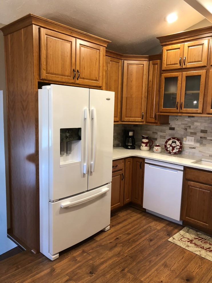 Mid-sized transitional u-shaped laminate floor and brown floor eat-in kitchen photo in Omaha with an undermount sink, raised-panel cabinets, medium tone wood cabinets, quartz countertops, beige backsplash, stone tile backsplash, white appliances and white countertops