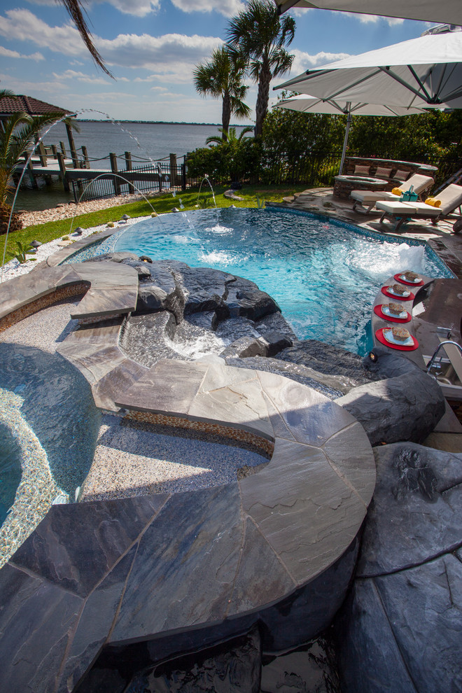 Design ideas for a tropical backyard custom-shaped pool in Houston with natural stone pavers.