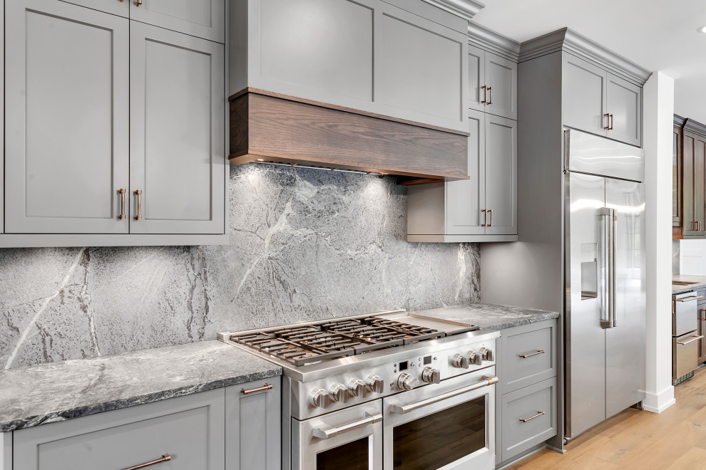 Example of a huge mountain style l-shaped medium tone wood floor, multicolored floor and wood ceiling eat-in kitchen design with an undermount sink, recessed-panel cabinets, gray cabinets, soapstone countertops, gray backsplash, quartz backsplash, stainless steel appliances, an island and gray countertops