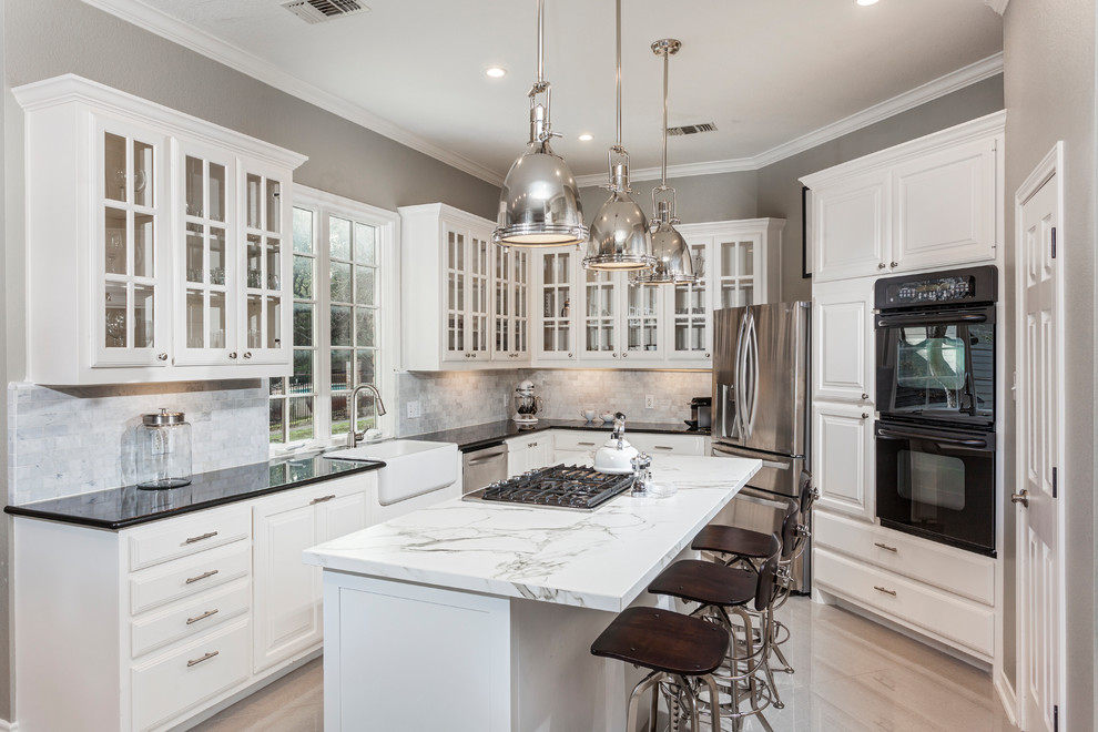 Inspiration for a traditional l-shaped kitchen in Austin with a farmhouse sink, glass-front cabinets, white cabinets, grey splashback, stainless steel appliances, light hardwood floors and with island.