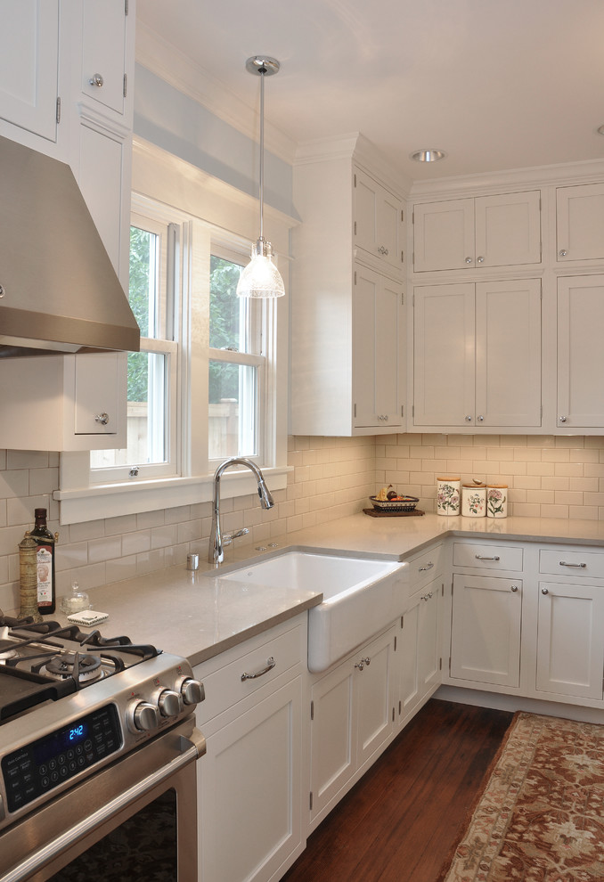 Photo of a mid-sized arts and crafts kitchen in Seattle with white cabinets, beige splashback, subway tile splashback, stainless steel appliances, dark hardwood floors, with island, a farmhouse sink, shaker cabinets and quartz benchtops.