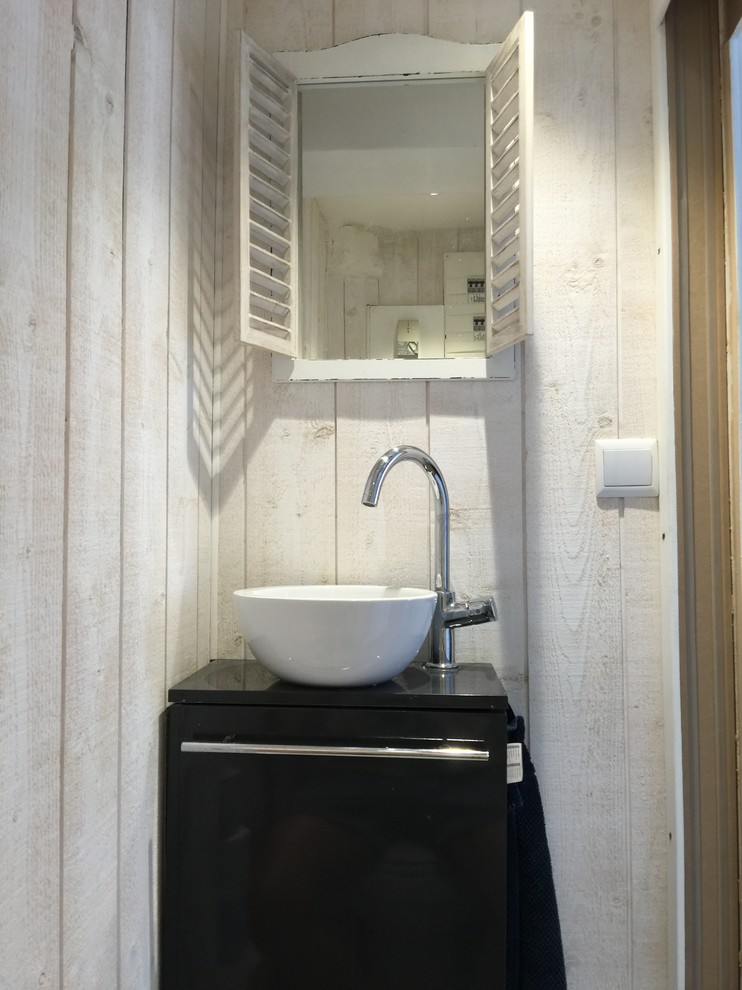 Photo of a small beach style powder room in Bordeaux with beaded inset cabinets, grey cabinets, a wall-mount toilet, beige walls, cement tiles, a vessel sink and grey floor.