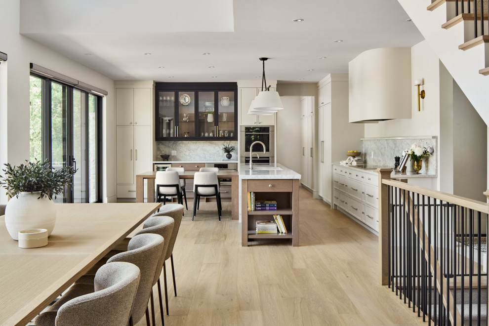 Example of a large transitional l-shaped light wood floor and brown floor eat-in kitchen design with a double-bowl sink, shaker cabinets, beige cabinets, quartz countertops, multicolored backsplash, quartz backsplash, stainless steel appliances, an island and white countertops