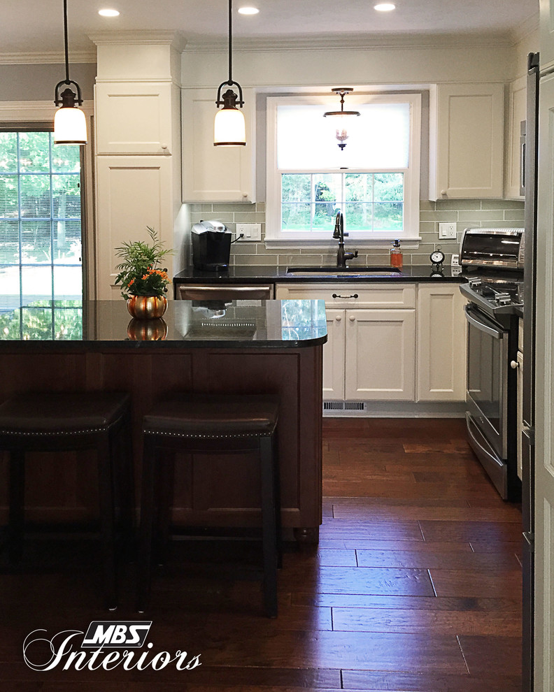 Example of a mid-sized transitional l-shaped medium tone wood floor and brown floor eat-in kitchen design with an undermount sink, white cabinets, granite countertops, gray backsplash, subway tile backsplash, stainless steel appliances, an island and recessed-panel cabinets