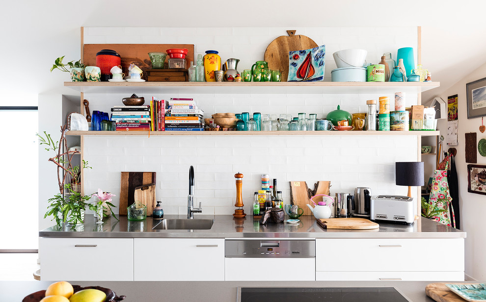 Photo of a modern galley kitchen in Sydney with an integrated sink, flat-panel cabinets, white cabinets, stainless steel benchtops, white splashback, subway tile splashback, with island and grey benchtop.