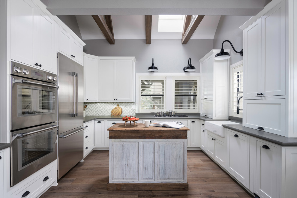 Design ideas for a mid-sized country u-shaped eat-in kitchen in Other with a farmhouse sink, shaker cabinets, white cabinets, quartz benchtops, grey splashback, porcelain splashback, stainless steel appliances, medium hardwood floors, with island, grey floor, grey benchtop and exposed beam.