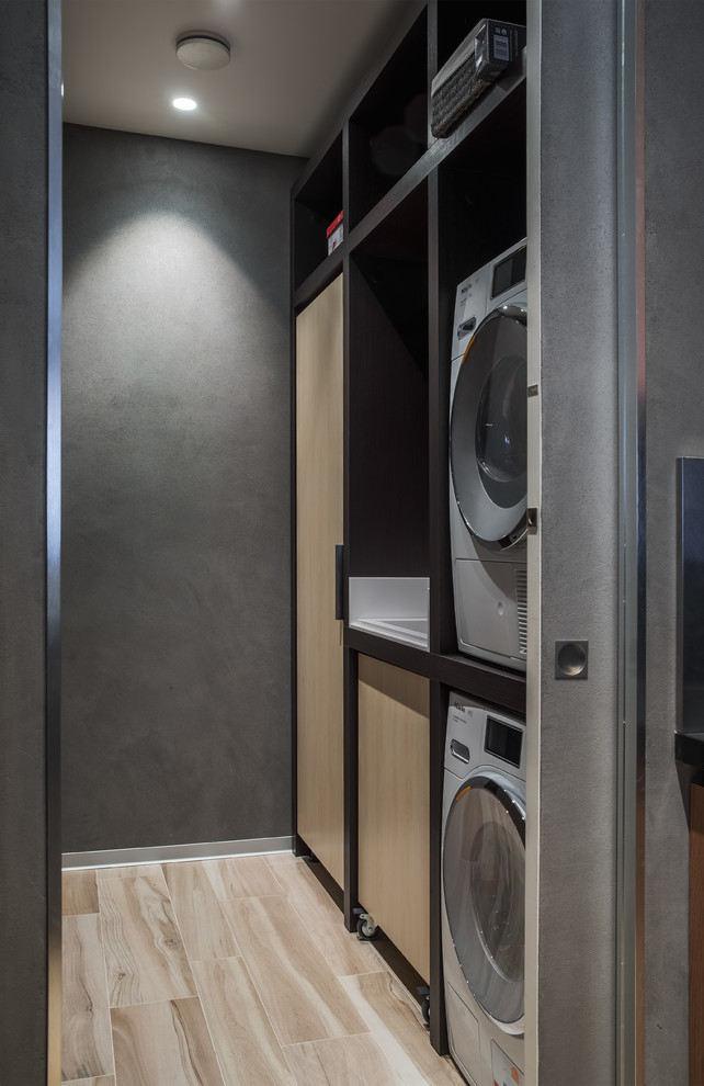 Inspiration for a small transitional dedicated laundry room in Moscow with an undermount sink, flat-panel cabinets, grey walls, porcelain floors, a stacked washer and dryer, beige floor and light wood cabinets.