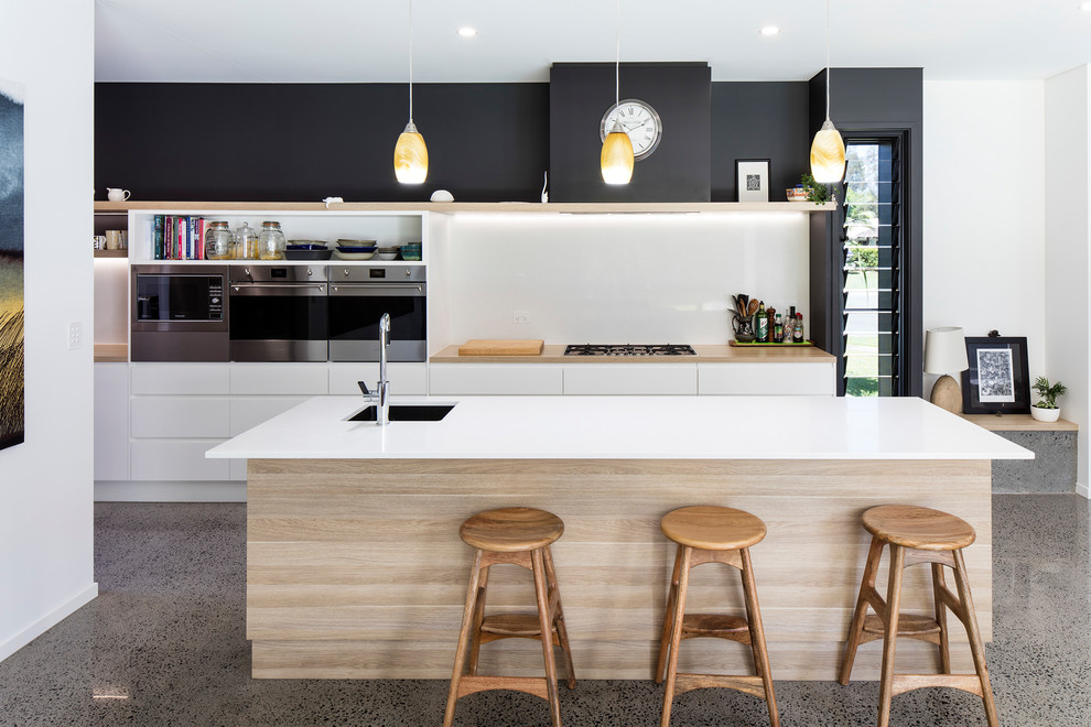 Photo of a contemporary galley eat-in kitchen in Sunshine Coast with an undermount sink, flat-panel cabinets, white cabinets, white splashback, stainless steel appliances, concrete floors, with island, grey floor and white benchtop.