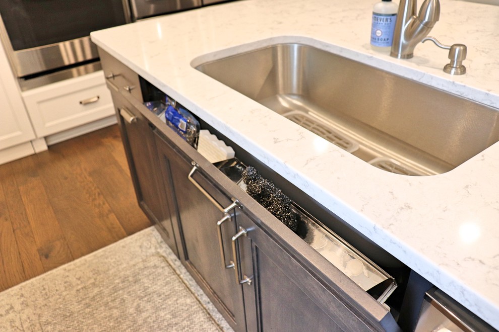 Transitional l-shaped medium tone wood floor and brown floor kitchen pantry photo in Cedar Rapids with an undermount sink, recessed-panel cabinets, white cabinets, quartzite countertops, gray backsplash, porcelain backsplash, stainless steel appliances, an island and white countertops