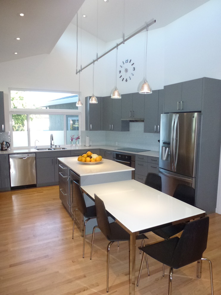 Photo of a large modern l-shaped eat-in kitchen in San Francisco with a double-bowl sink, flat-panel cabinets, grey cabinets, quartz benchtops, grey splashback, glass tile splashback, stainless steel appliances, light hardwood floors and with island.